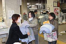 女性2人が支援物資として寝具を職員へ提供している写真