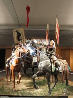 相馬野馬追(そうまのまおい)の中の、神旗争奪戦ジオラマ。黒い馬、茶色い馬にそれぞれ乗って、背に旗を掲げた2人の武将が戦っている様子が再現されています。