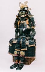 黒漆塗鳩胸五枚胴具足の写真。金の飾りがついた黒い兜。全身の鎧も黒い、腰かけた姿の全身用の甲冑が飾られている写真です。