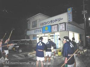コインランドリーの前で鉢巻と法被姿の男性たちが柄杓で水をかけている様子