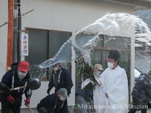 榊を持った宮司が歩いているところに沿道の人が水をかけているところ