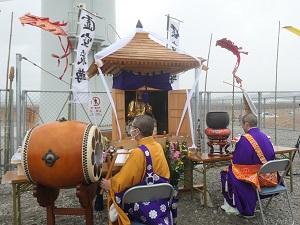 御本尊を納めた厨子の前で僧侶が二人座って祈りを捧げている。一人の僧侶は和太鼓を叩いている。