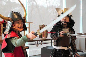 体験用の甲冑と陣羽織を着た男の子二人がおもちゃの刀を持ってポーズしている