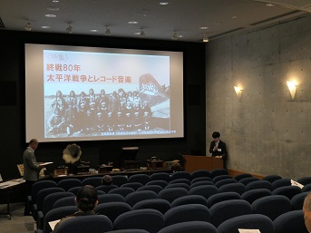 スクリーンの前で説明をする博物館の学芸員