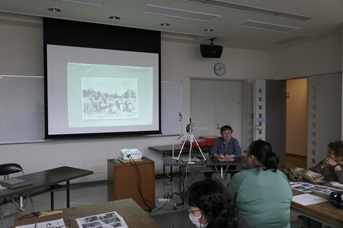 スクリーンに写真を映して解説する参加者とそれを聞くほかの参加者たち
