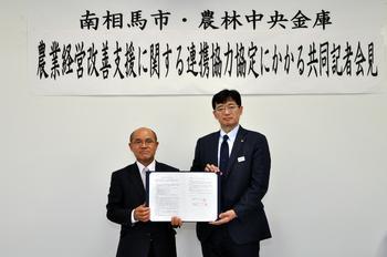 共同記者会見で桜井市長と有田支店長が連携協力締結を交わし協定書を二人で持っている写真