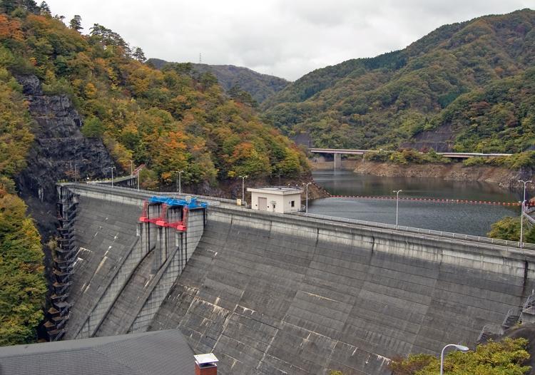 どんよりした曇り空の中、後方が木々に囲まれている横川ダムを正面から撮影した風景写真。