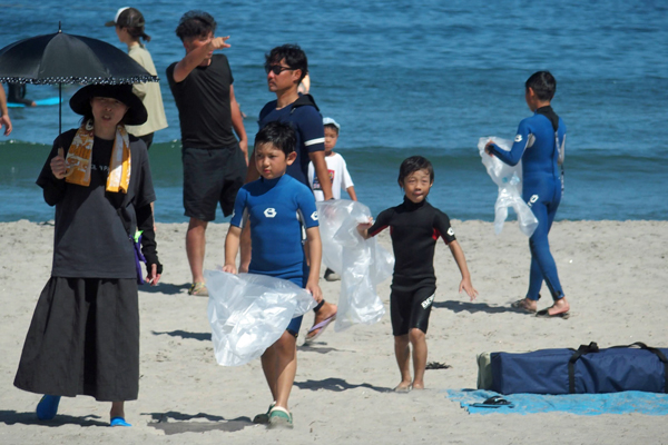 ゴミ袋を持ってビーチを歩く子供たちの写真