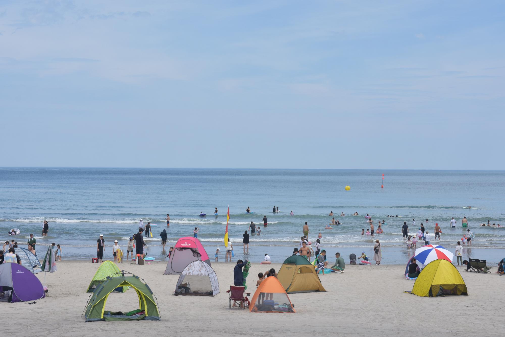 海岸にビーチパラソルなどが並び多くの人が海水浴をしている写真