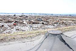 道路が陥没した為マンホールが隆起し、奥には津波で全てが攫われた後の瓦礫だけが残されている写真