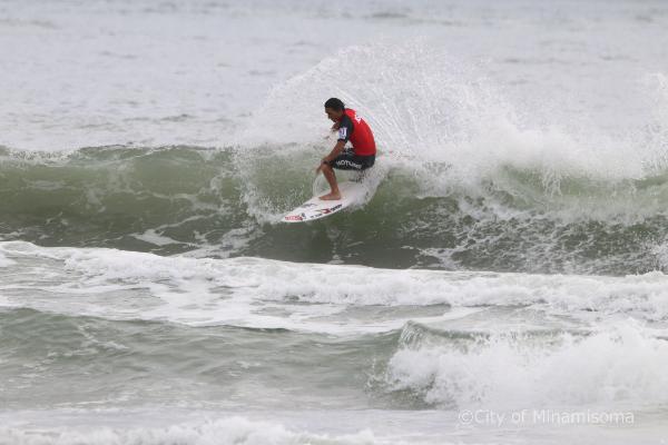 赤いウエアを着用した選手が水しぶきを上げながら波に乗る写真