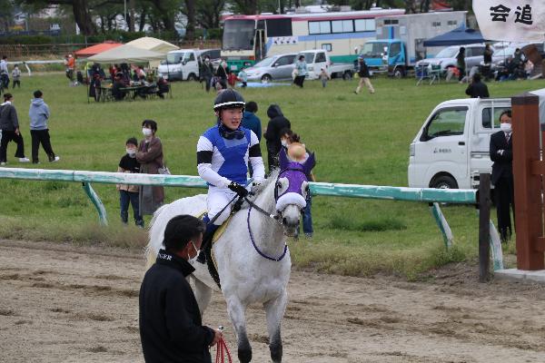青い勝負服を着た騎手が乗馬している写真