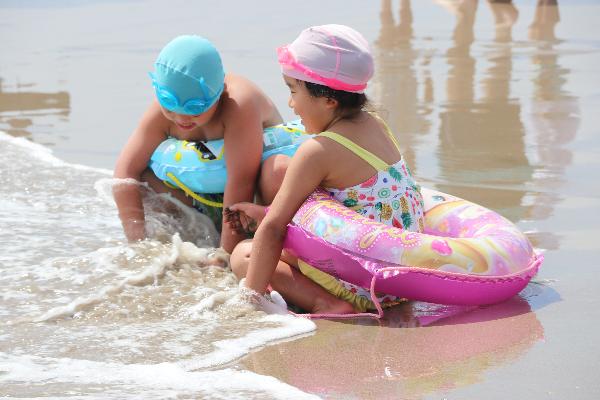浮き輪を付けた二人の子供が、波打ち際で遊ぶ様子を撮影した写真