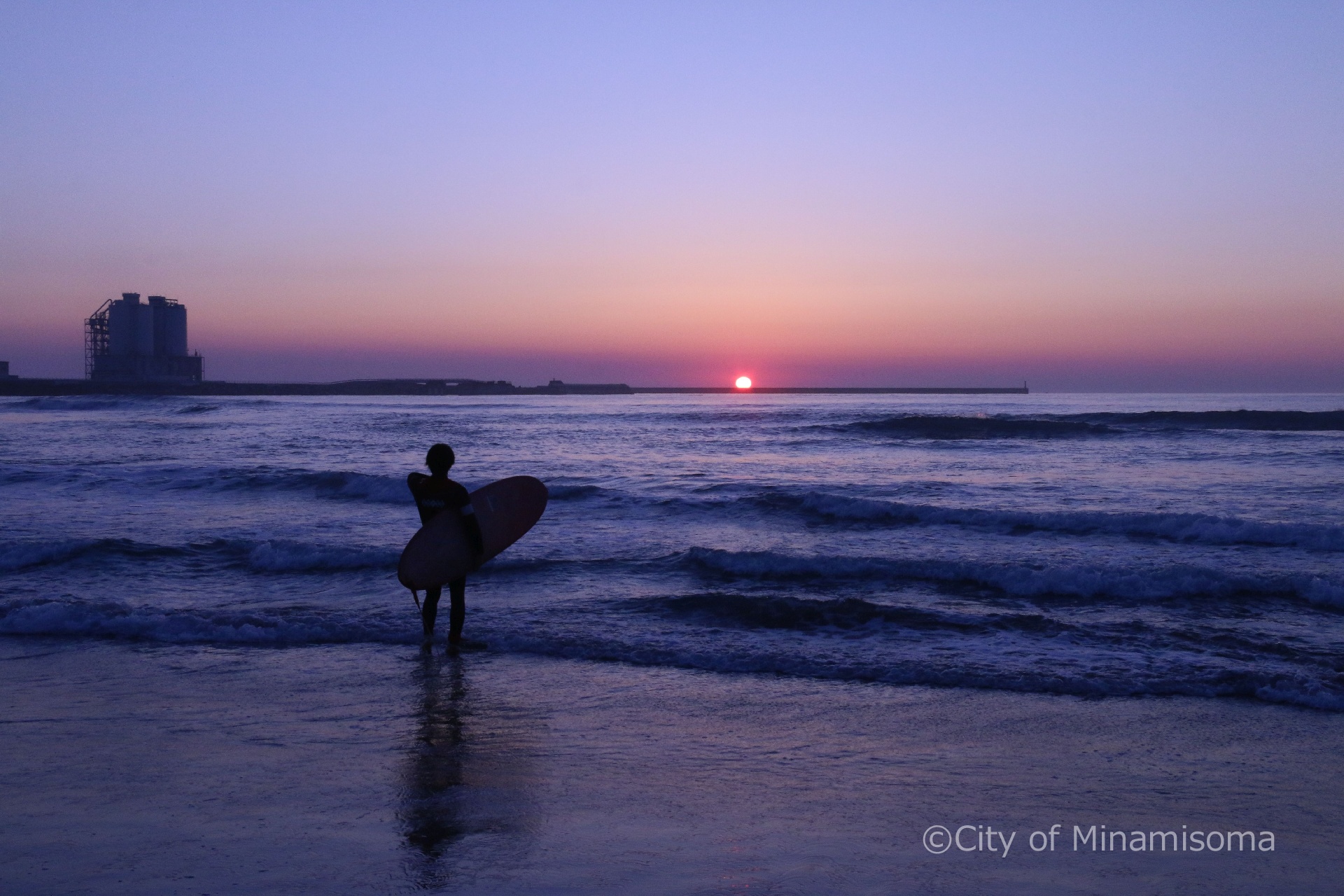 原町区北泉の海岸の様子。夏の夜明け、サーフィンを持った男性のシルエットが朝焼けの海に浮かび上がる。