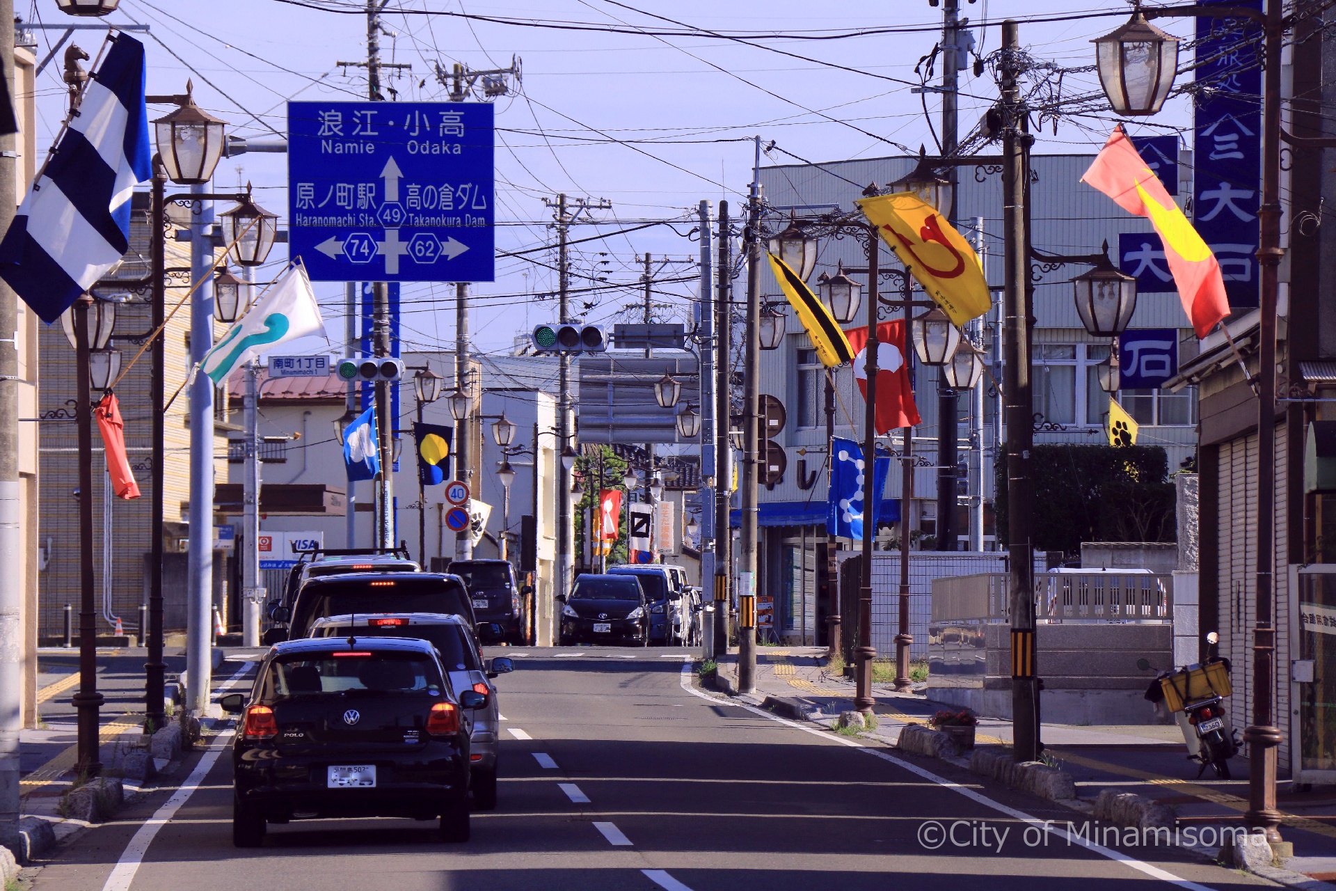 相馬野馬追直前の町の様子。車が走っている道路脇の街灯に、旗指物が飾られている。