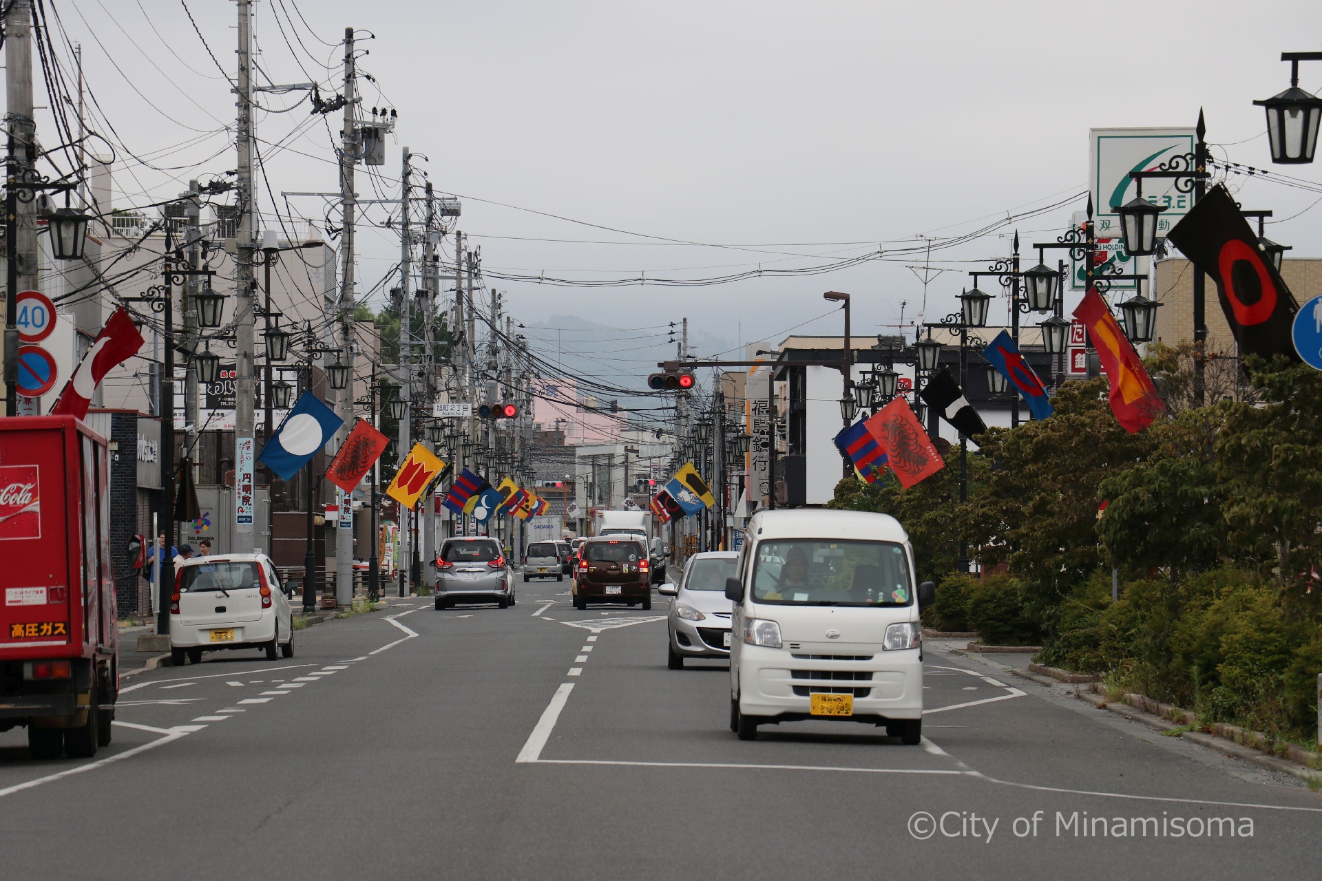 原ノ町駅前を車が走っている様子。野馬追開催前で、道路脇の街灯には旗指物が飾られている。