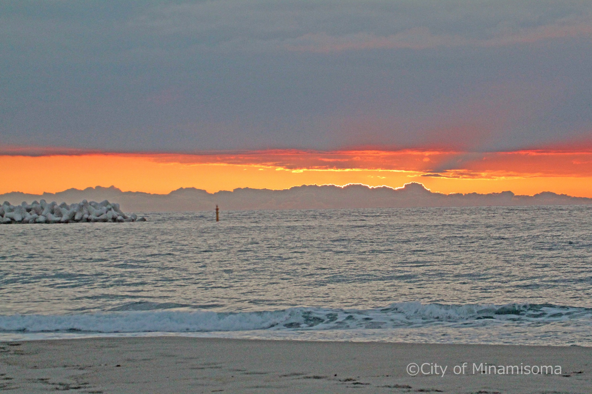 早朝の烏崎海岸。灰色の雲と海の間に見える空が、オレンジ色の帯のように見える。