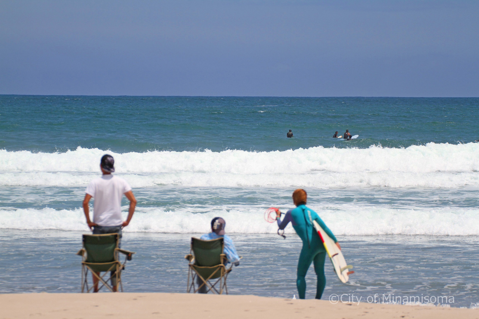 北泉海岸でサーフィンをする人と、砂浜でそれを見ている人の様子。