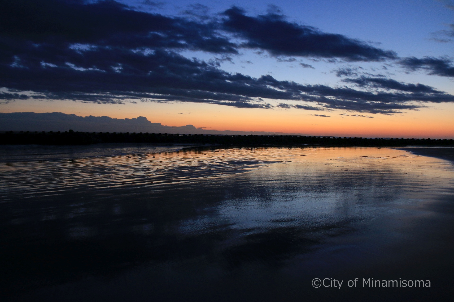 早朝の北泉海岸の様子。青とオレンジのグラデーションの空が、波打ち際に映っている。