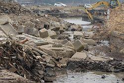 津波によって石で積み上げた堤防が決壊し、流木が積み上がっている写真