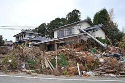 2階建て住居の1階部分を埋め尽くす津波で流されてきた瓦礫の山となぎ倒され屋根にめり込んだ電柱の写真