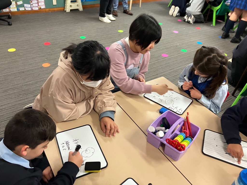 現地校の子供たちと話したり名前を書いたりする学生たちの写真