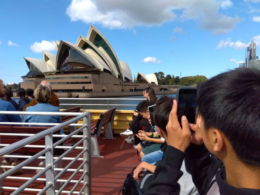 フェリーからオペラハウスの写真を撮る学生の写真