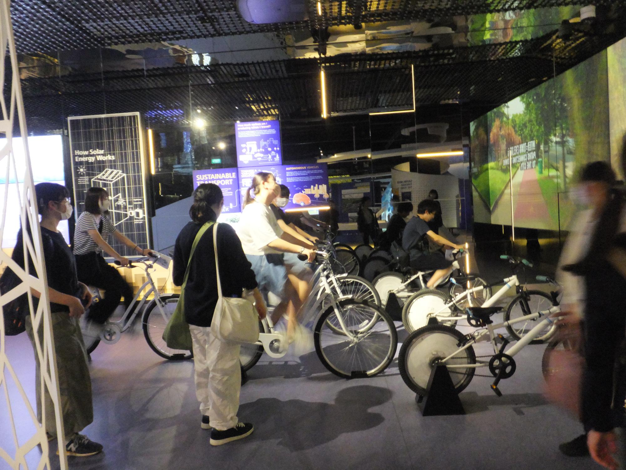 屋内で自転車による発電を体験している学生の写真