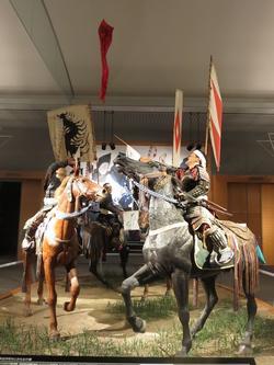 相馬野馬追（そうまのまおい）の中の、神旗争奪戦ジオラマ。黒い馬、茶色い馬にそれぞれ乗って、背に旗を掲げた2人の武将が戦っている様子が再現されています。