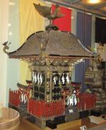 太田神社の神輿の写真。室内に飾られた状態。頂きに羽ばたいた鳳凰が飾られた木製の神輿です。