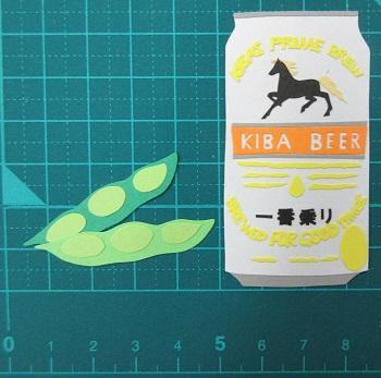 枝豆と缶ビールの切り絵。ビールのラベルが馬になっており、KIBA BEER、一番乗り、とある