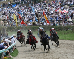 雲雀ヶ原の馬場で4頭の馬と騎手が甲冑競馬をしていてたくさんの見物客いる様子
