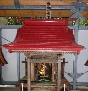 牛頭天皇と立札の付いた赤い屋根の祠にキュウリが供えられている