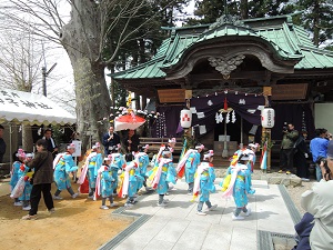 青い着物を着て、笠を被った子どもたちが神社の前で踊りを踊っている様子