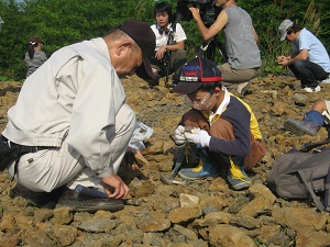 ゴーグルをした男の子が大人の男性と一緒にしゃがんで掘った石を見ている様子
