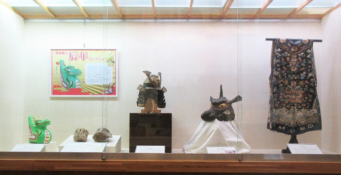 硝子戸のケースの中に辰の張り子人形やクジラの椎骨化石2つ、兜などの資料が展示してある様子。