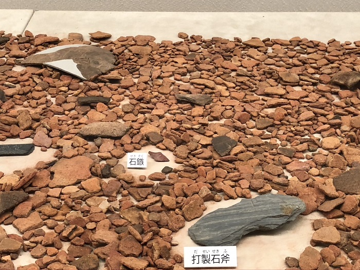 たくさんの土器の破片の中に打製石斧や石鏃が置かれている展示