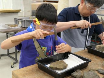 ゴーグルをかけた少年がハンマーとタガネで石を割っているところ
